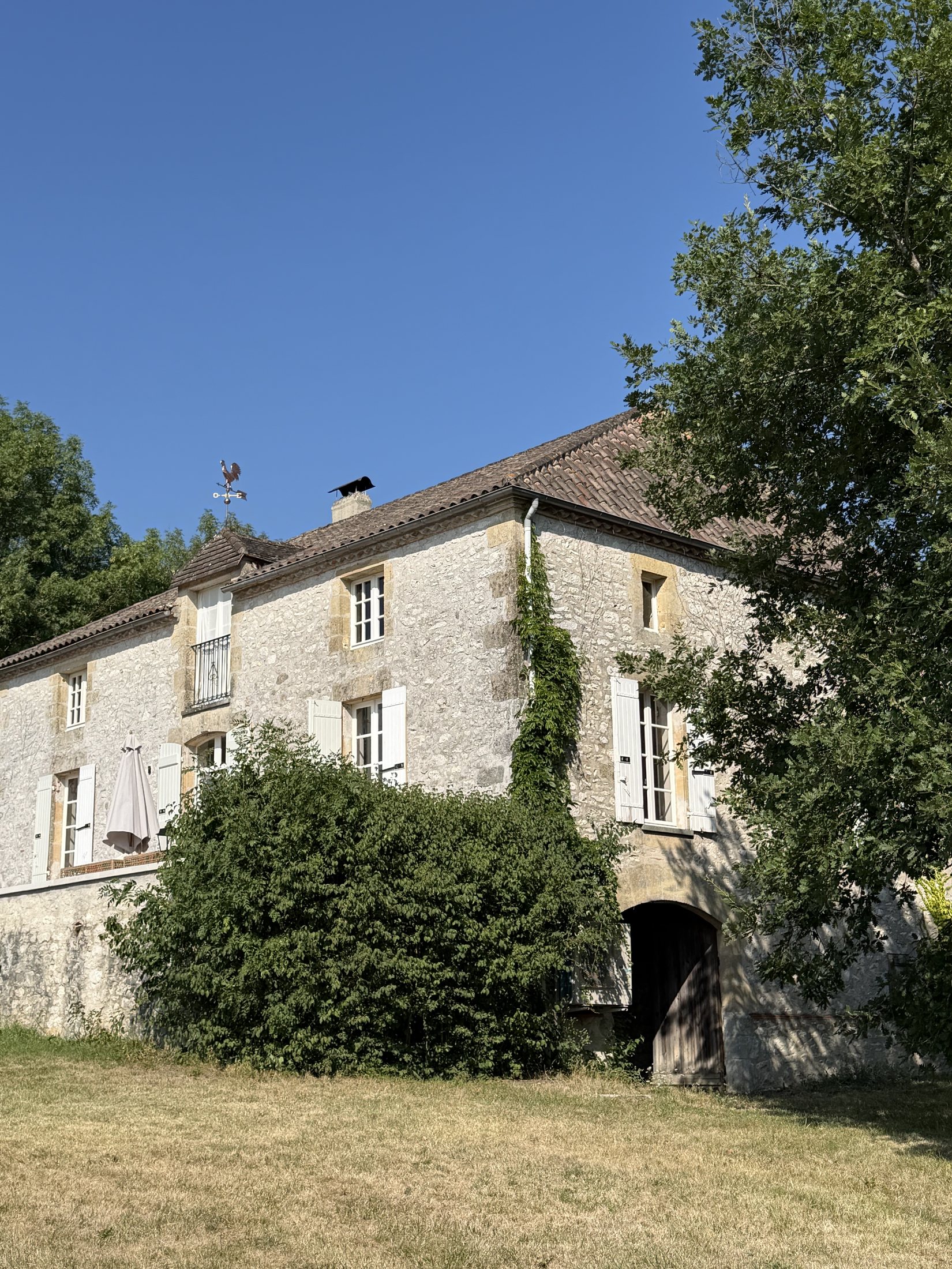 Die Natursteinfassade des Manoir Comté zwischen alten Bäumen
